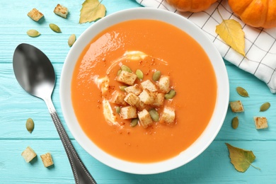 Photo of Tasty creamy pumpkin soup with croutons and seeds in bowl on light blue wooden table, flat lay