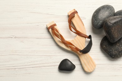 Photo of Slingshot with stones on white wooden table, flat lay. Space for text