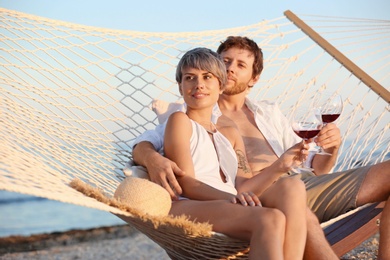 Young couple resting with glasses of wine in hammock on beach