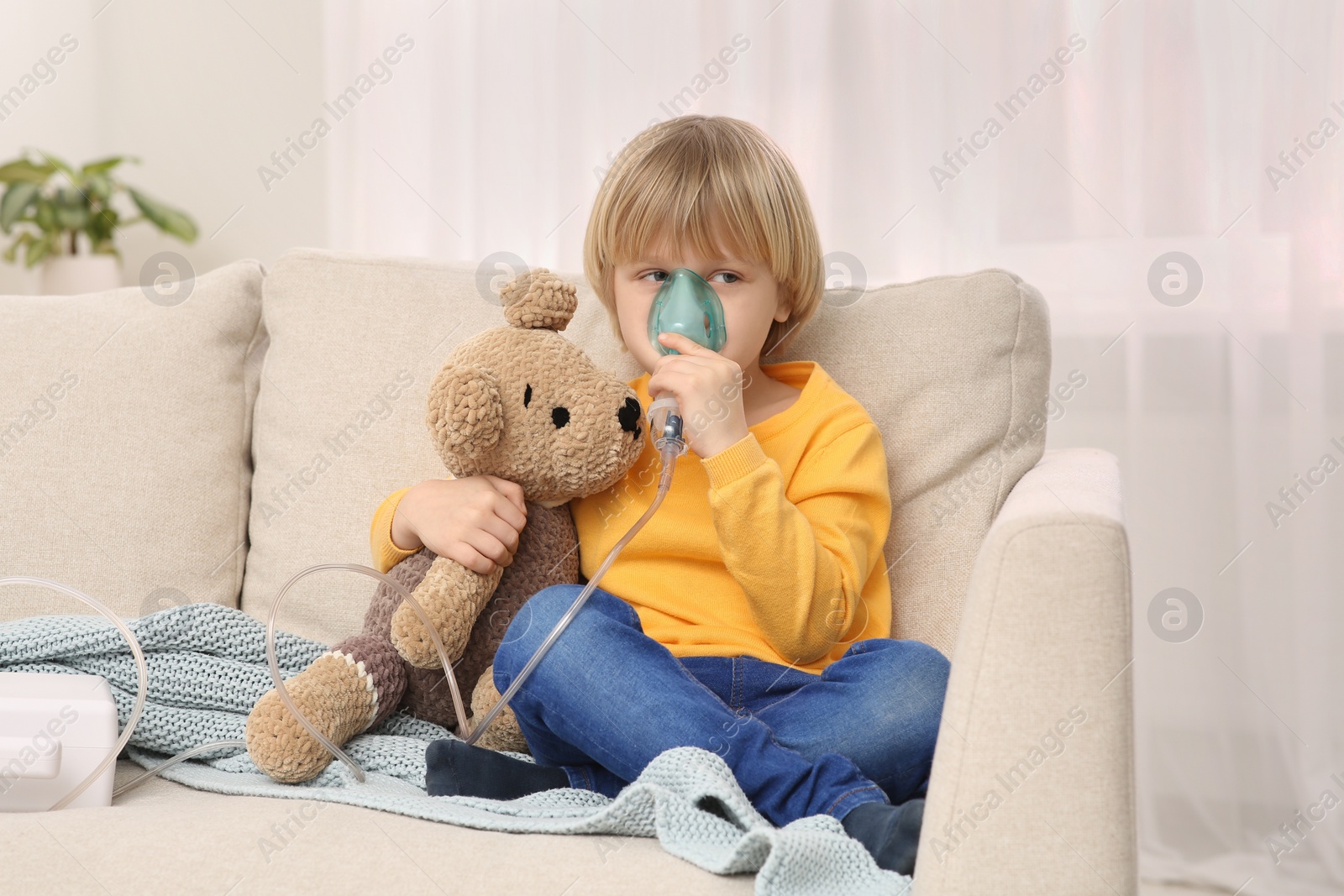 Photo of Boy with toy bear using nebulizer for inhalation at home