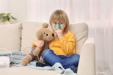 Boy with toy bear using nebulizer for inhalation at home