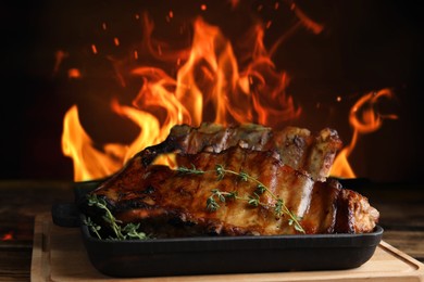 Image of Tasty grilled ribs with thyme on wooden board and bright flame on background