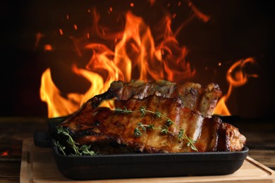 Tasty grilled ribs with thyme on wooden board and bright flame on background