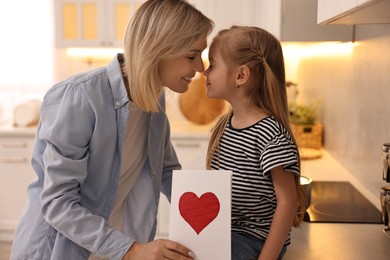 Photo of Little daughter congratulating her mom with greeting card in kitchen. Happy Mother's Day