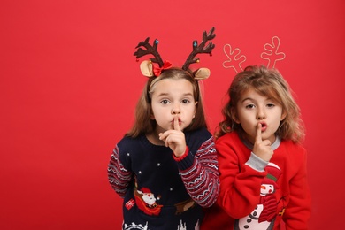 Photo of Kids in Christmas sweaters and festive headbands on red background, space for text