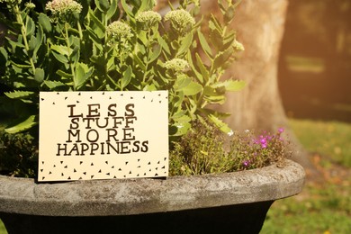 Photo of Card with phrase Less Stuff More Happiness on stone planter outdoors, space for text