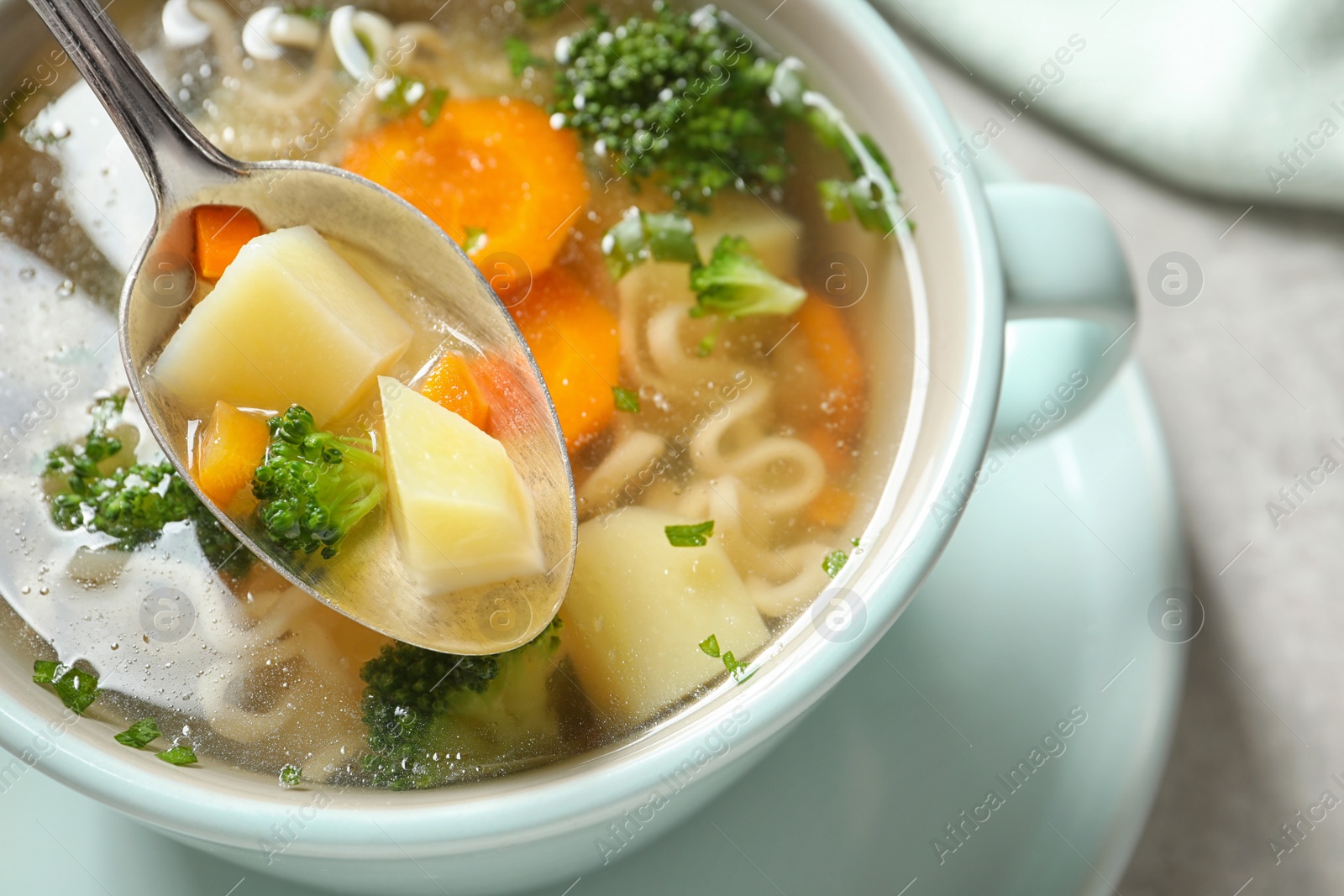 Photo of Spoon of fresh homemade vegetable soup over full dish on table, closeup