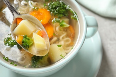 Spoon of fresh homemade vegetable soup over full dish on table, closeup