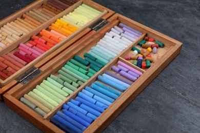 Photo of Set of colorful pastels in wooden box on grey stone table, closeup. Drawing materials