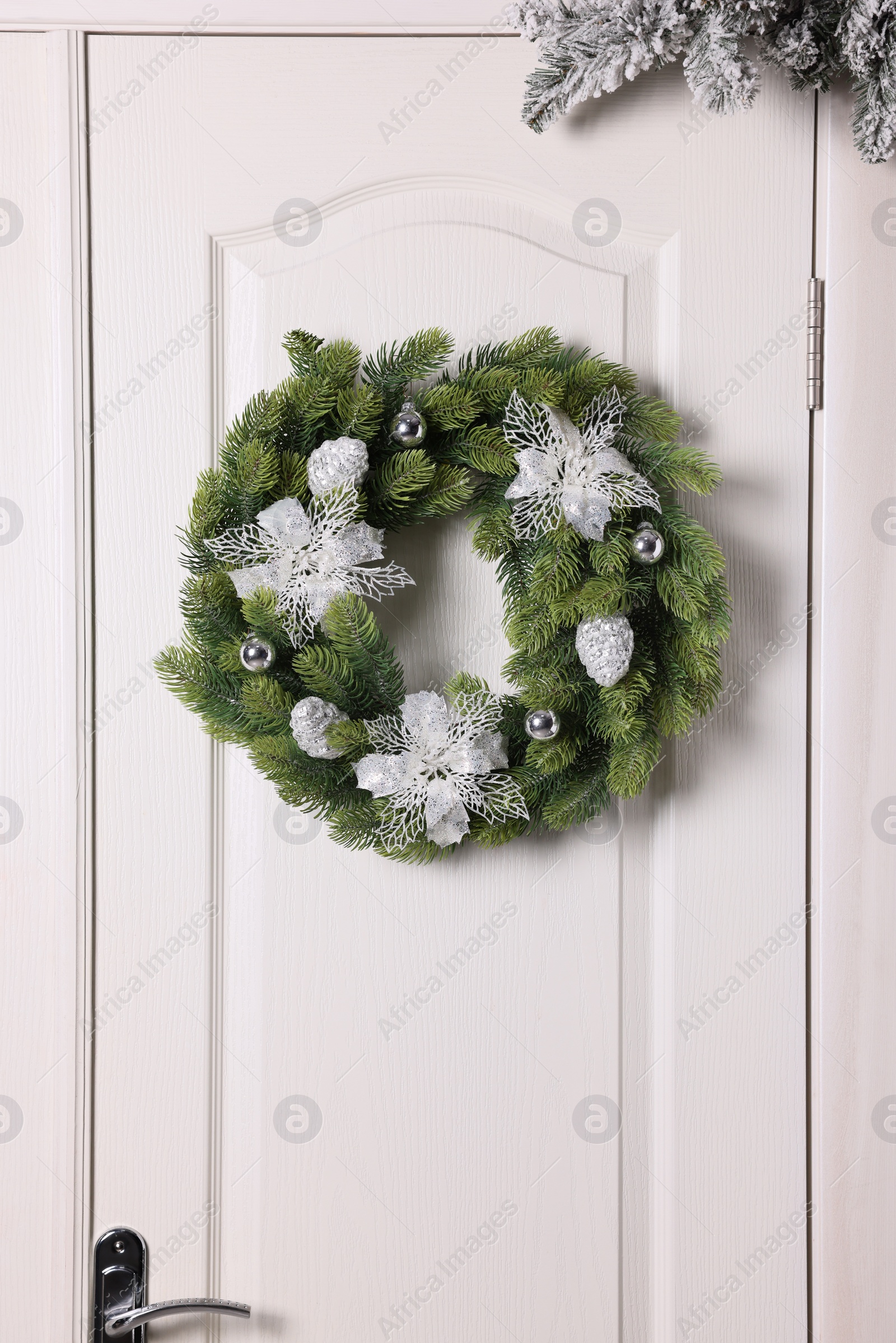 Photo of Beautiful Christmas wreath with festive decor hanging on white door