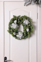 Beautiful Christmas wreath with festive decor hanging on white door