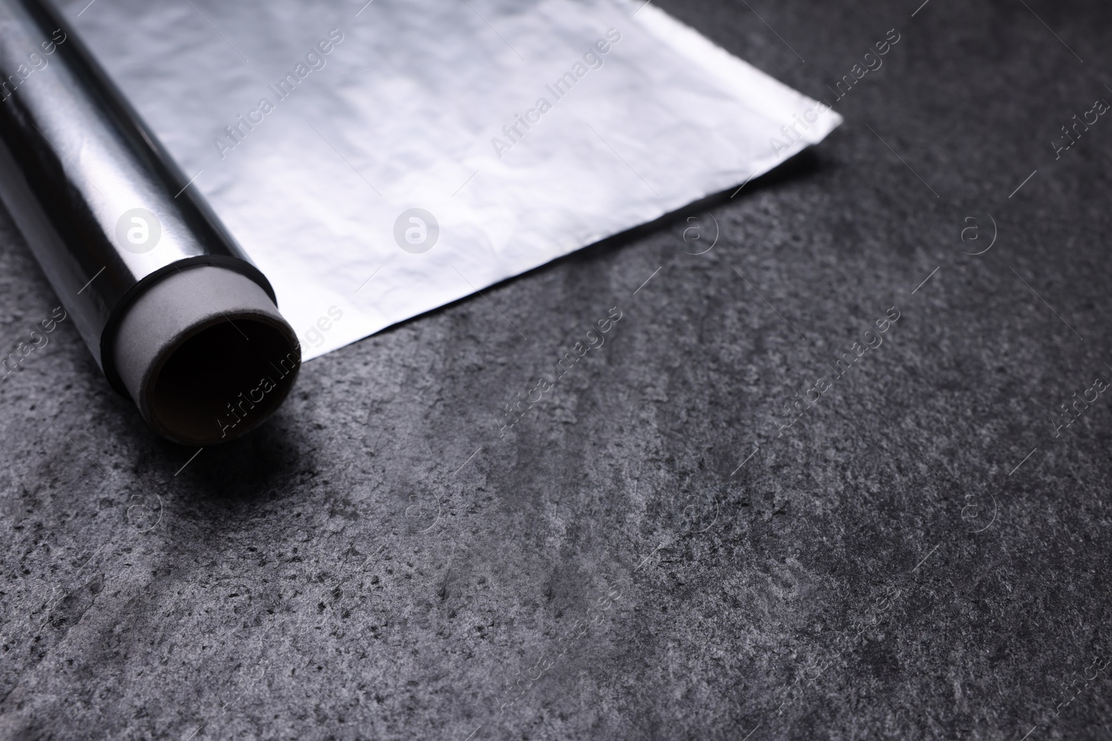 Photo of Roll of aluminum foil on grey table, closeup. Space for text