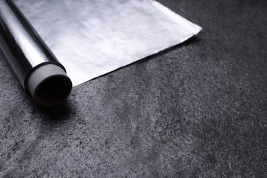 Roll of aluminum foil on grey table, closeup. Space for text