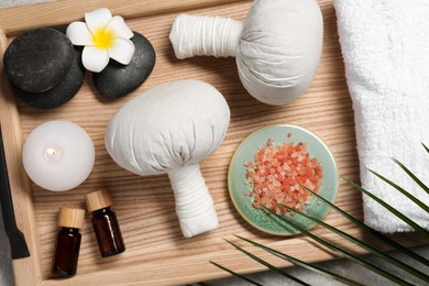 Herbal massage bags, spa stones, sea salt and essential oils on grey table, flat lay
