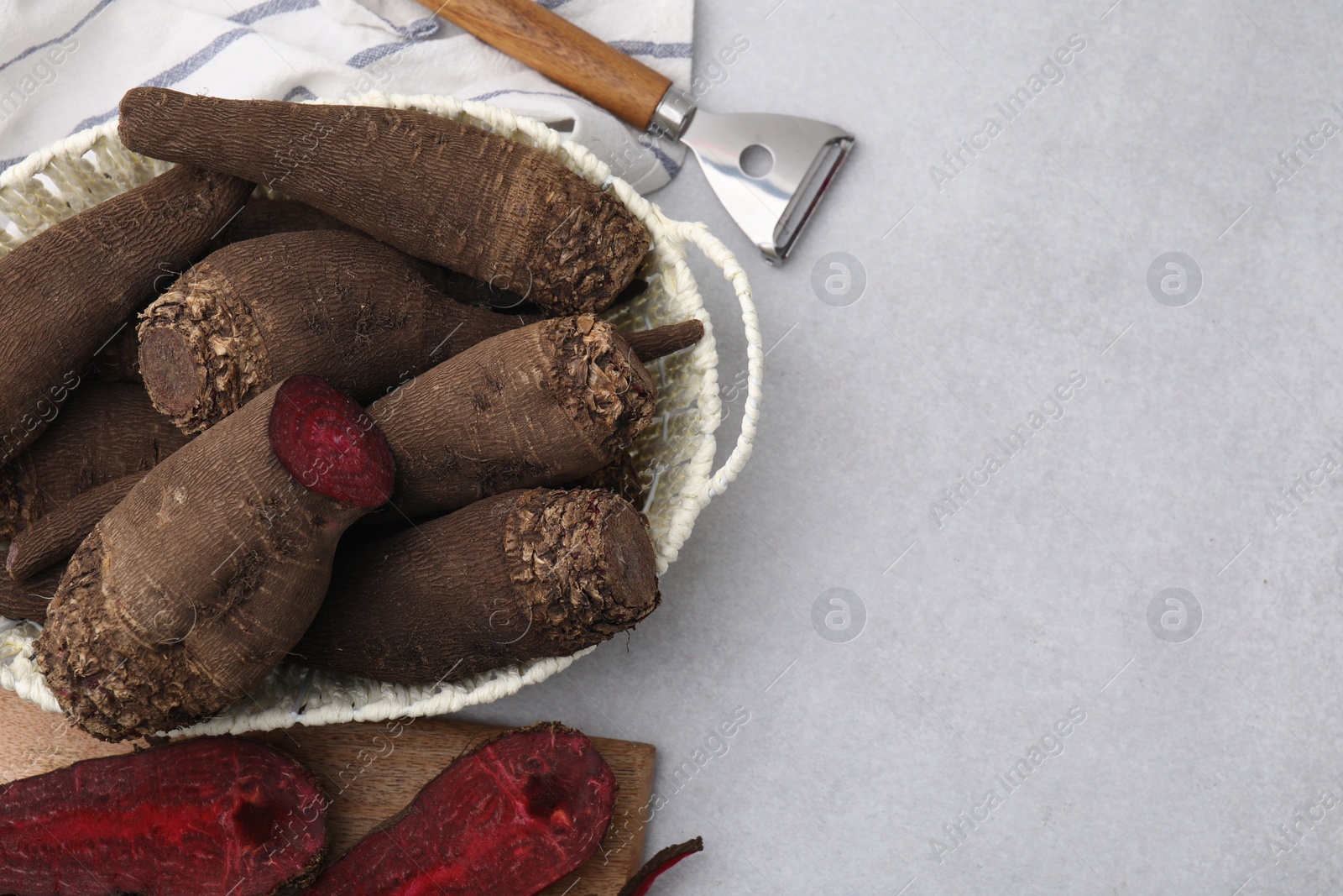 Photo of Basket with whole, cut red beets and vegetable peeler on light gray table, flat lay. Space for text