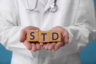 Doctor holding wooden cubes with abbreviation STD on light blue background, closeup