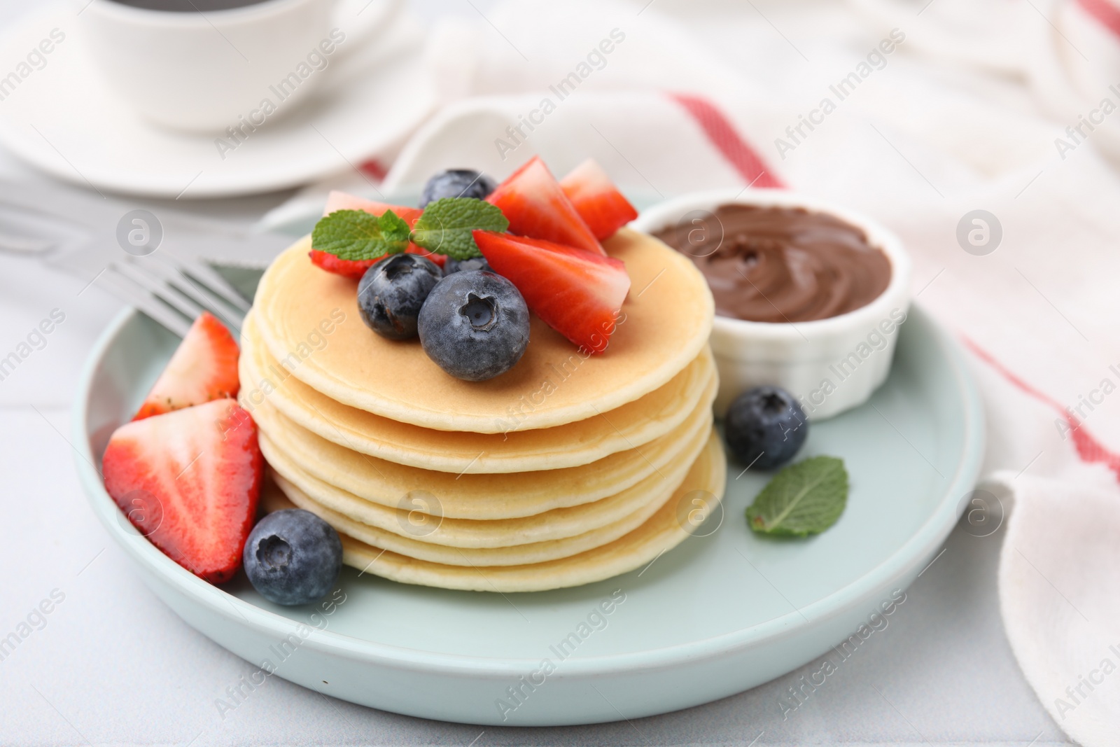 Photo of Delicious pancakes with strawberries, blueberries and chocolate sauce on light table, closeup