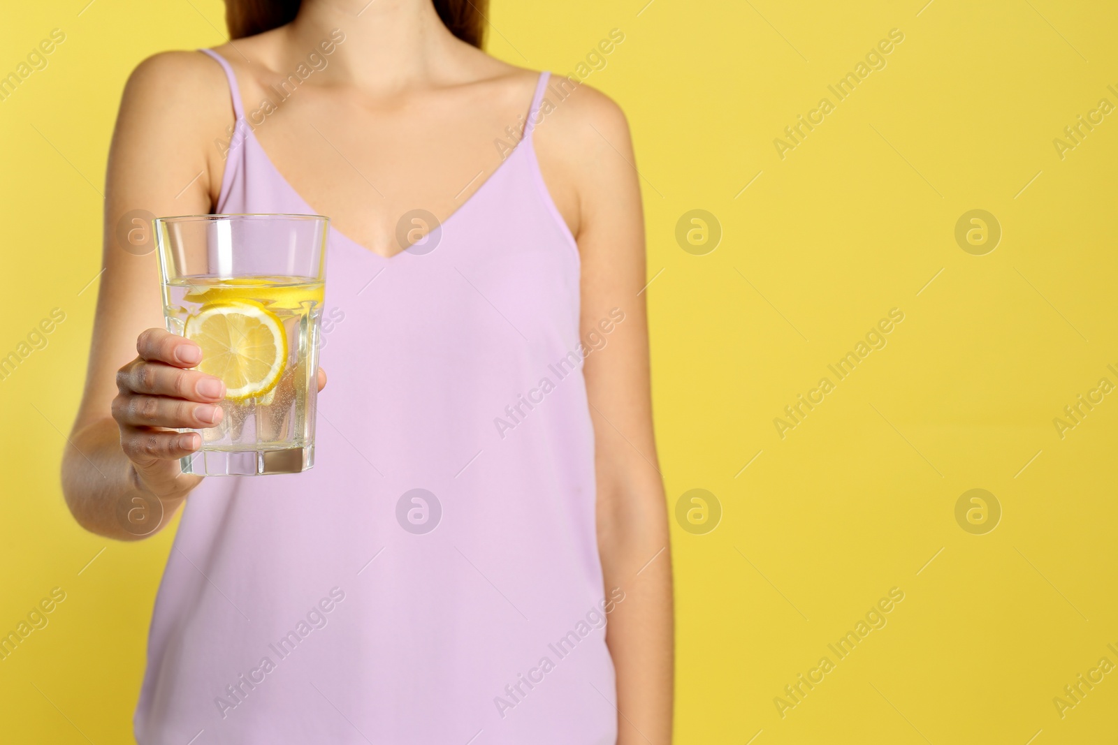 Photo of Young woman with glass of lemon water on yellow background, closeup. Space for text