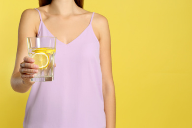 Photo of Young woman with glass of lemon water on yellow background, closeup. Space for text