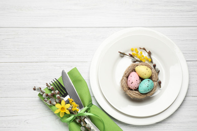 Festive Easter table setting with quail eggs and floral decor on white wooden background, flat lay