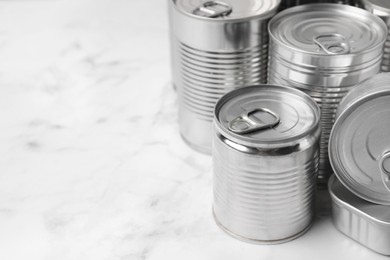 Many closed tin cans on white marble table, closeup. Space for text