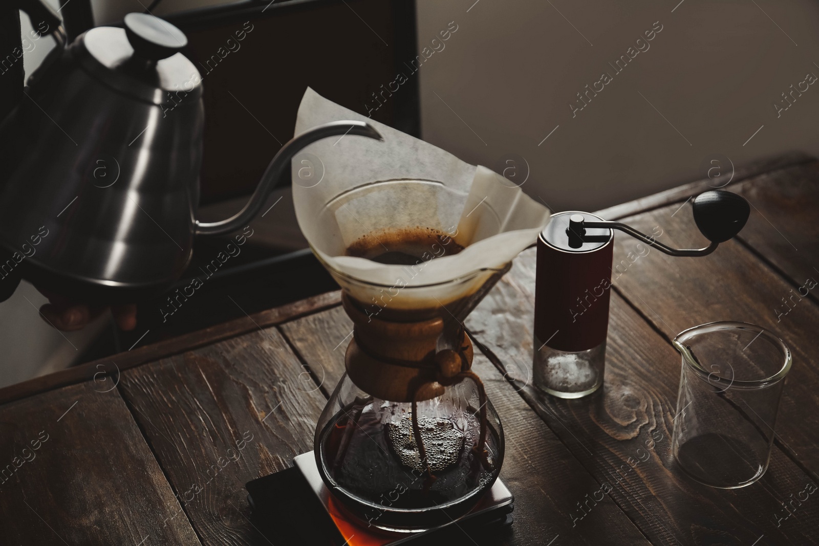 Photo of Barista pouring hot water into coffee maker at wooden table in cafe, closeup