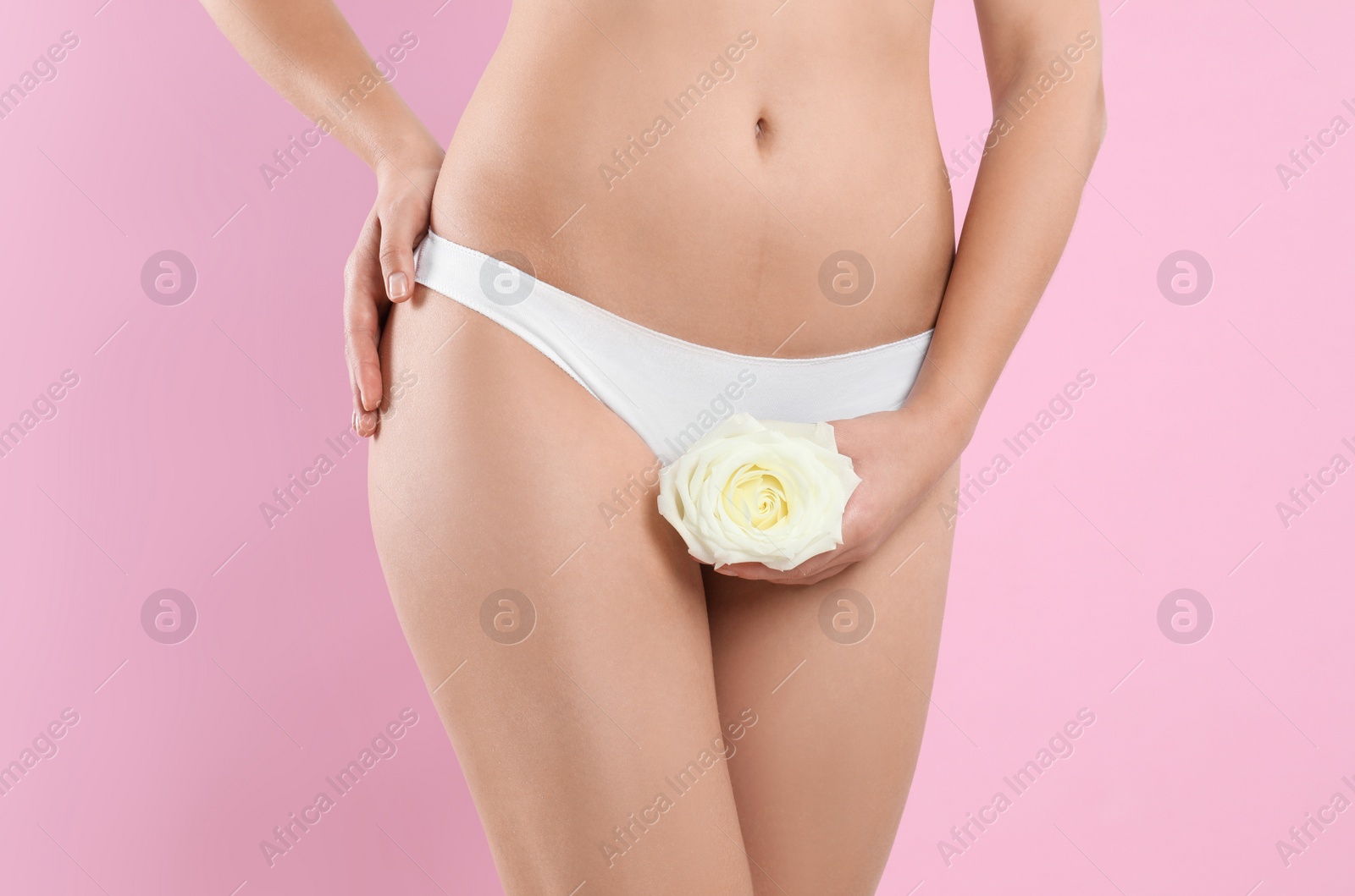 Photo of Woman with rose showing smooth skin on pink background, closeup. Brazilian bikini epilation