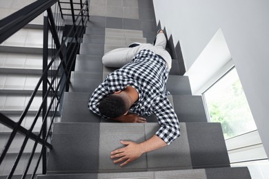 Photo of Unconscious man lying on stairs after falling down indoors, top view