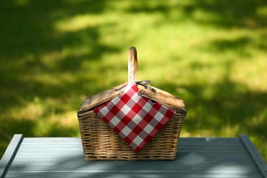 Photo of Wicker basket with blanket on table in park. Summer picnic