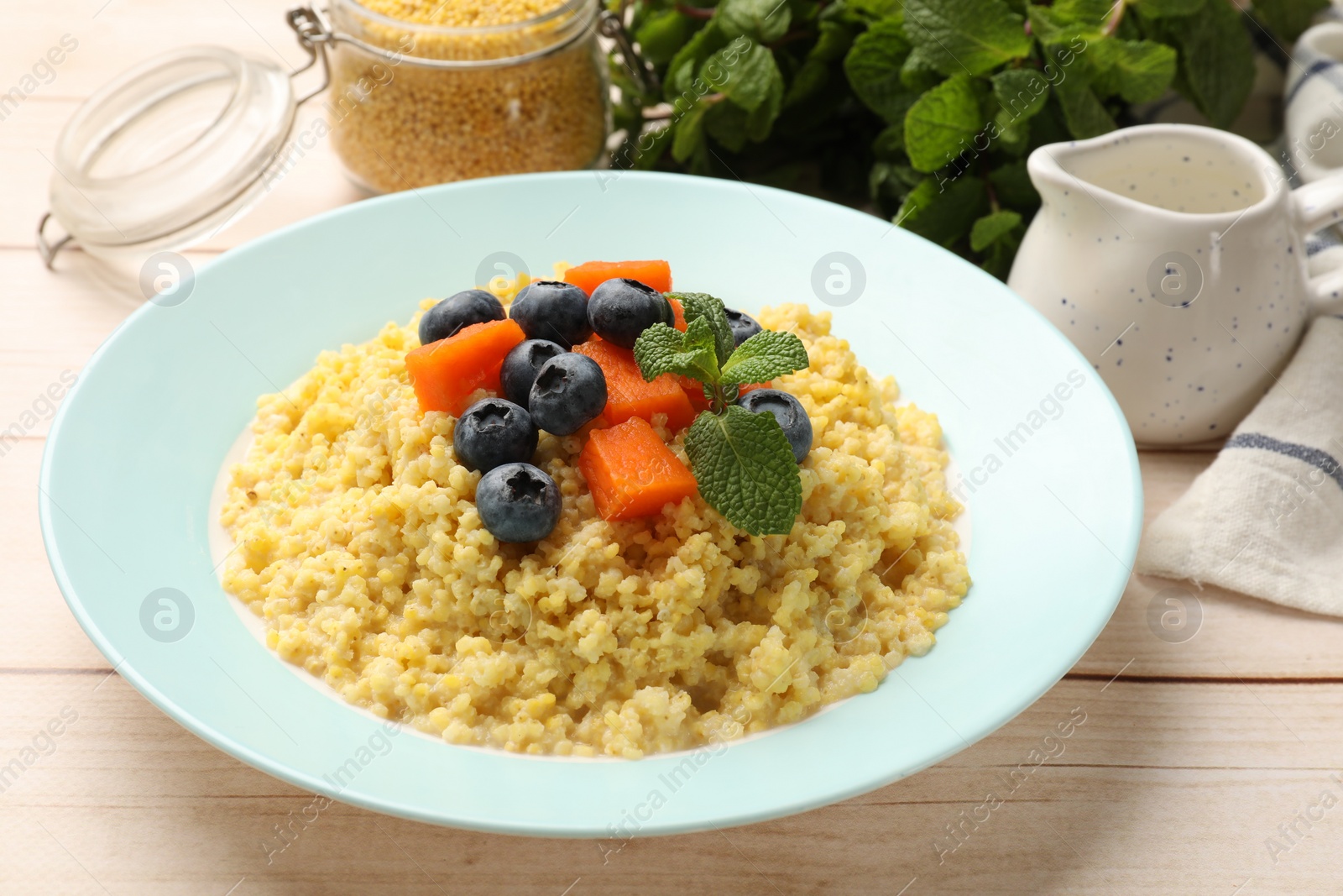 Photo of Plate with tasty millet porridge, blueberries, pumpkin and mint on light wooden table, closeup