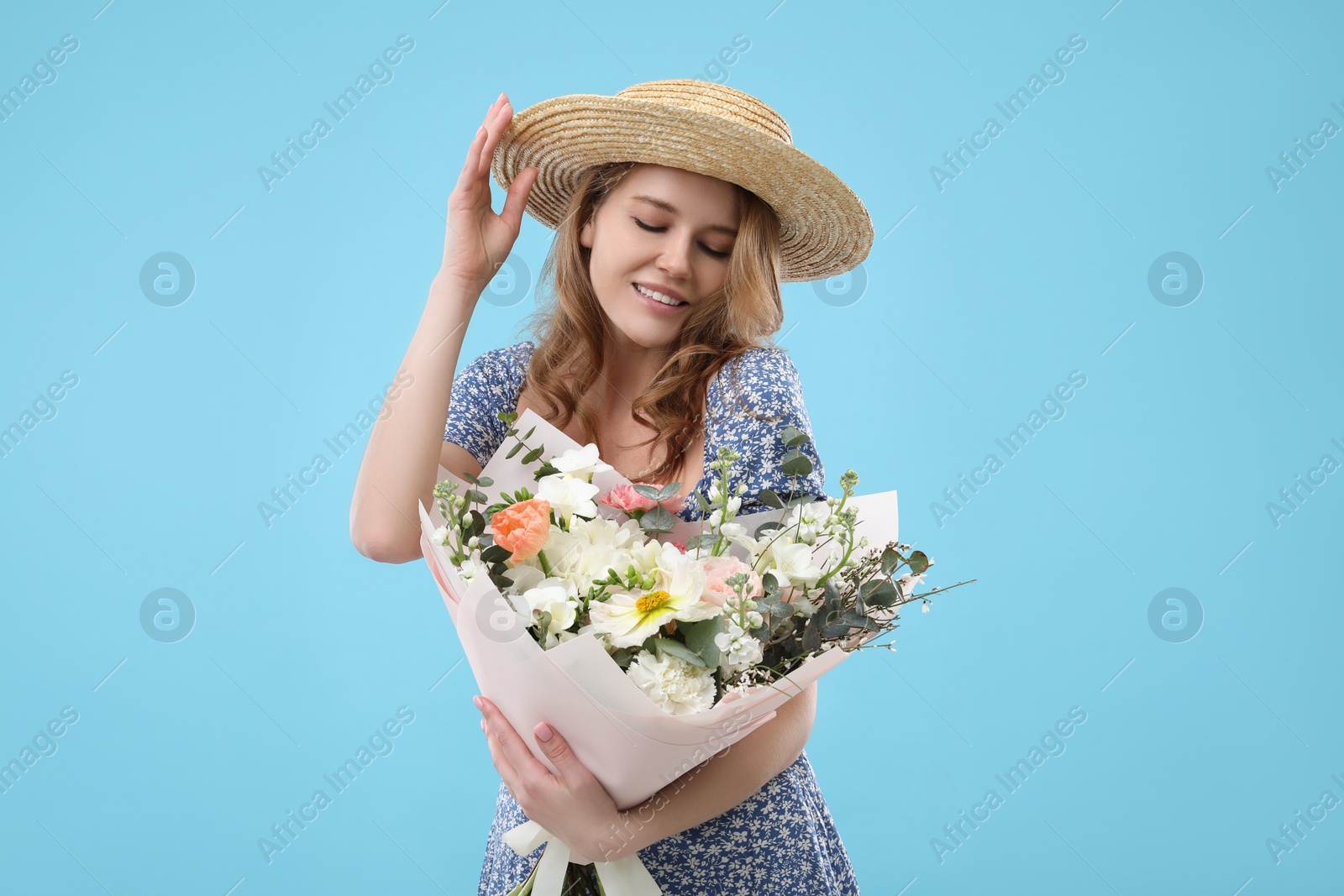 Photo of Beautiful woman in straw hat with bouquet of flowers on light blue background