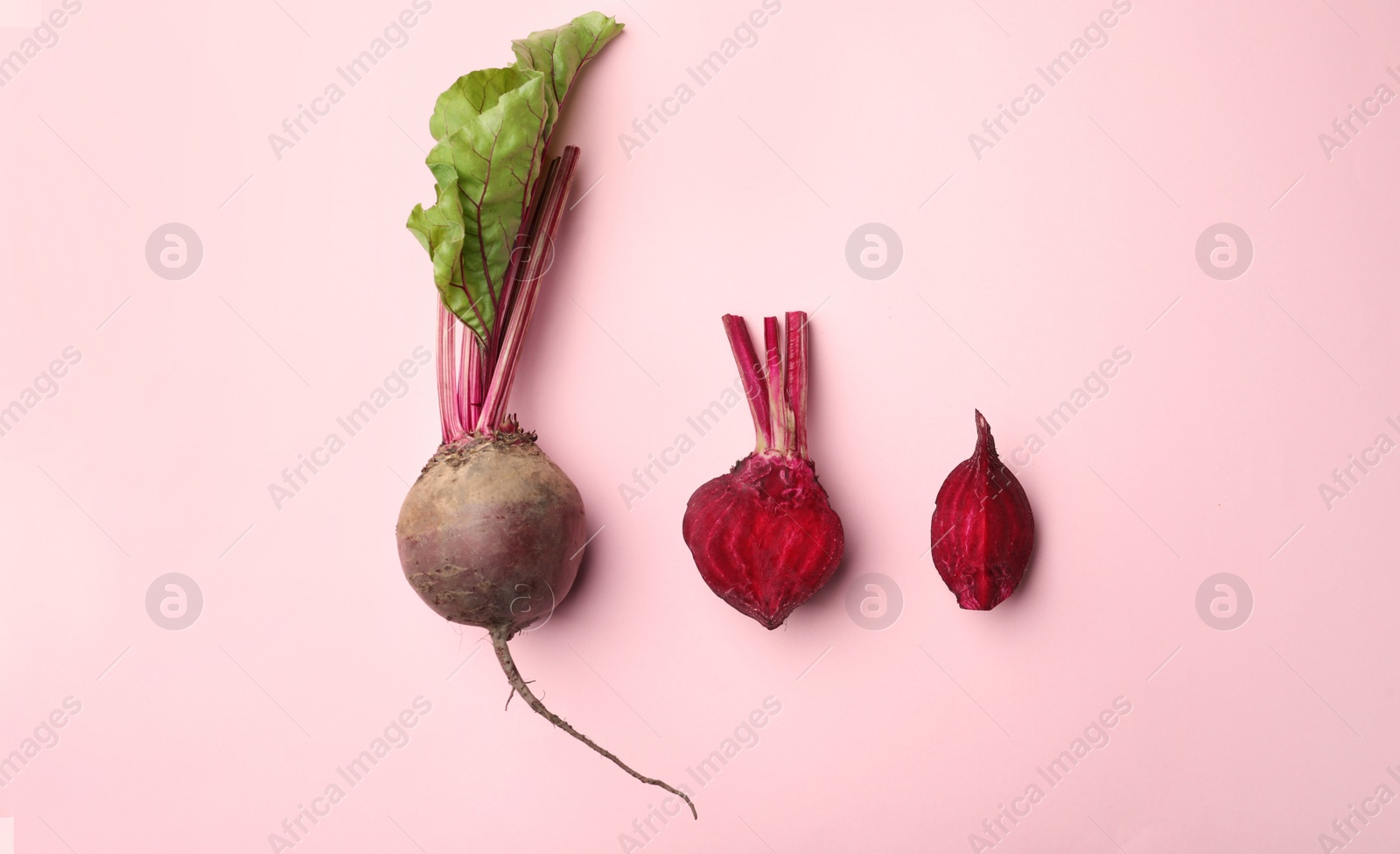 Photo of Whole and cut fresh red beets on pink background, flat lay