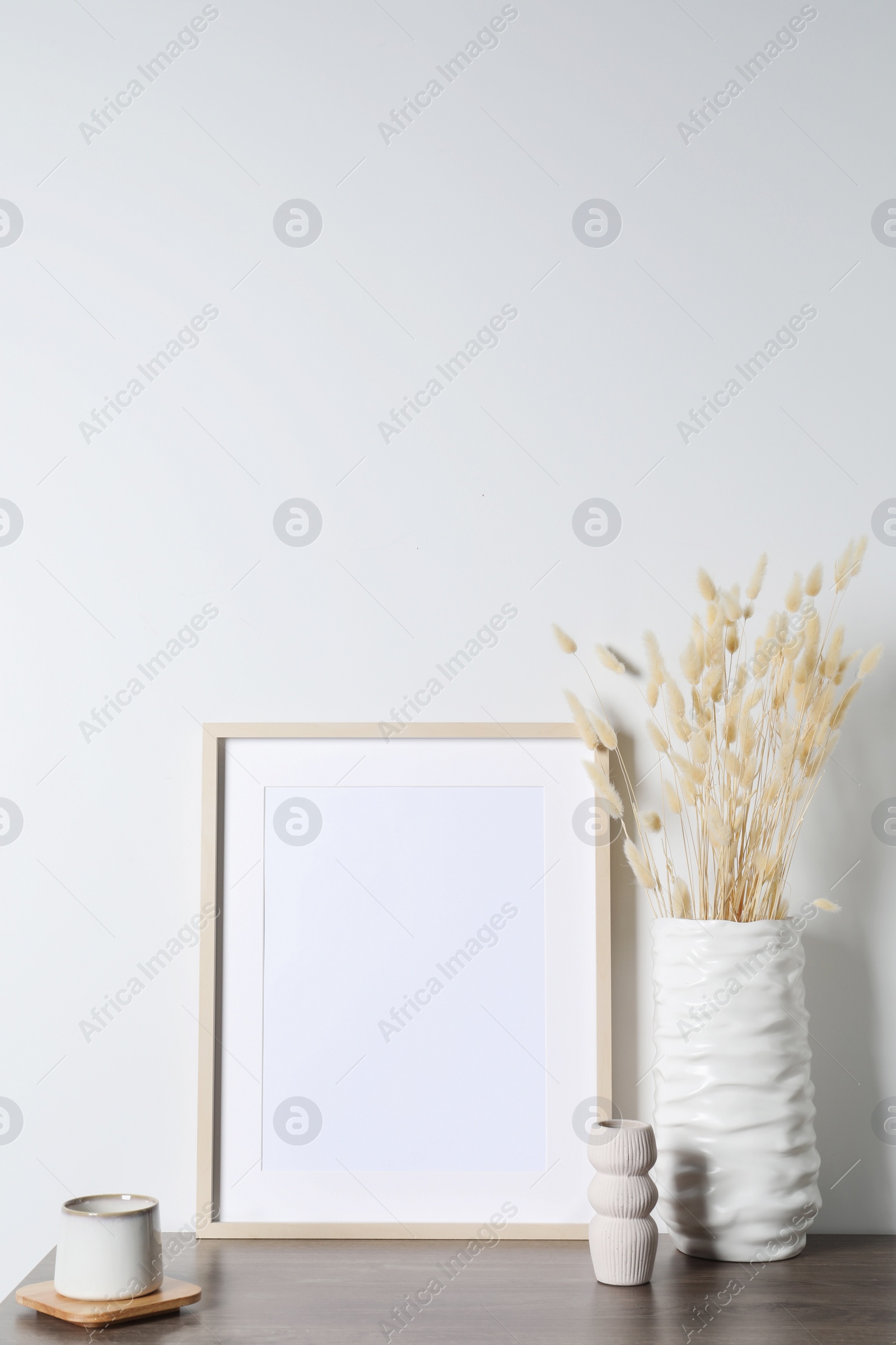 Photo of Empty photo frame, cup and vase with dry decorative spikes on wooden table. Mockup for design