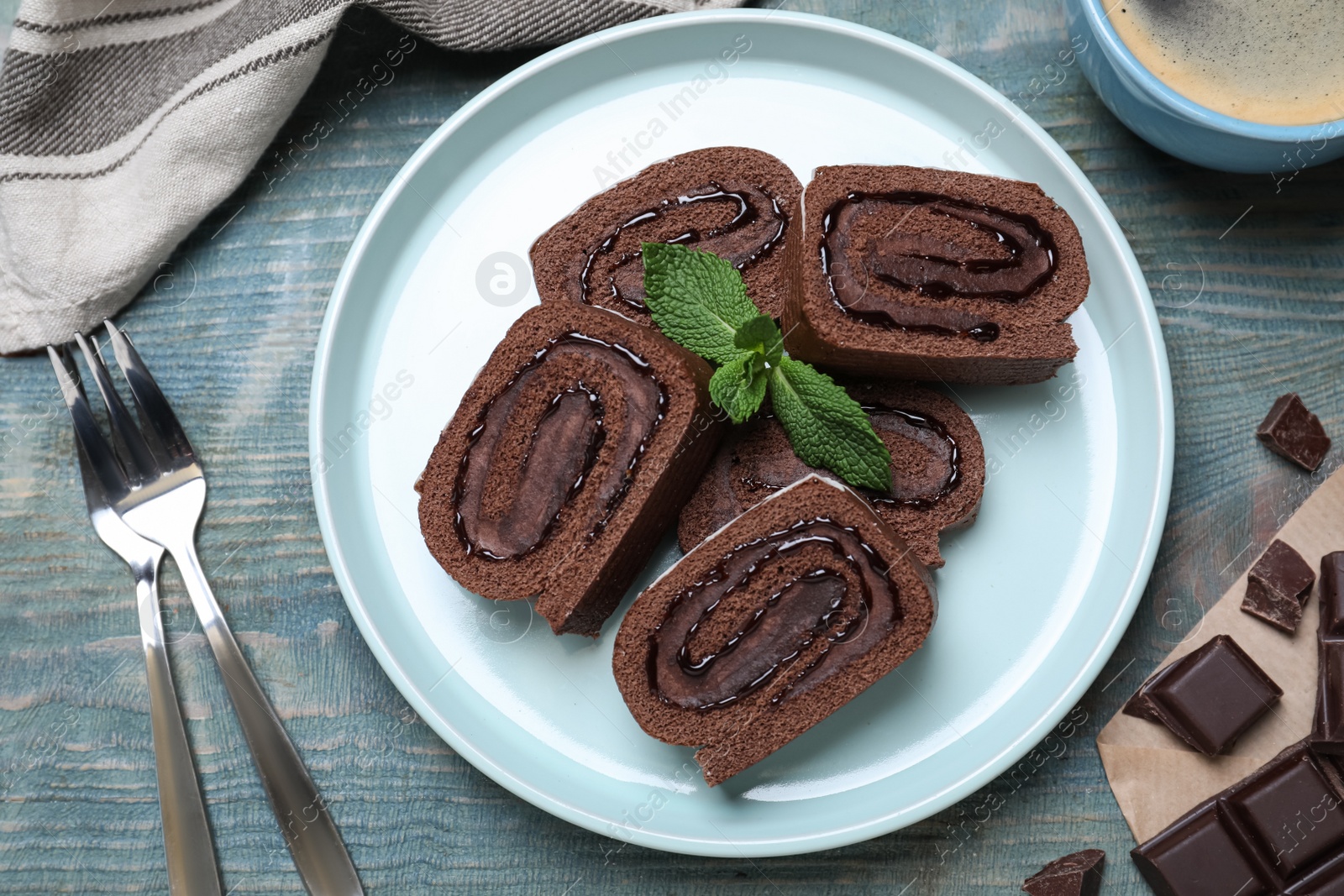 Photo of Tasty chocolate cake roll with cream and mint on blue wooden table, flat lay