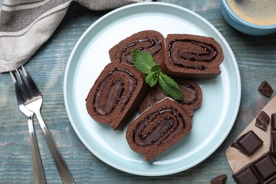 Photo of Tasty chocolate cake roll with cream and mint on blue wooden table, flat lay