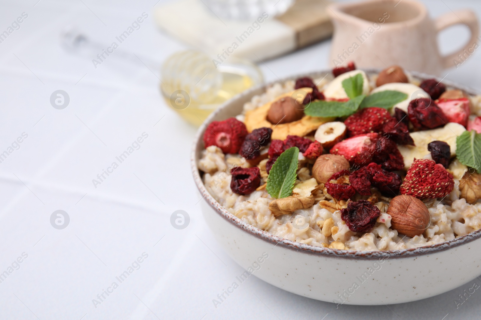 Photo of Oatmeal with freeze dried fruits, nuts and mint on white wooden table, closeup. Space for text