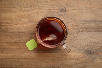 Photo of Tea bag in glass cup of hot water on wooden table, top view