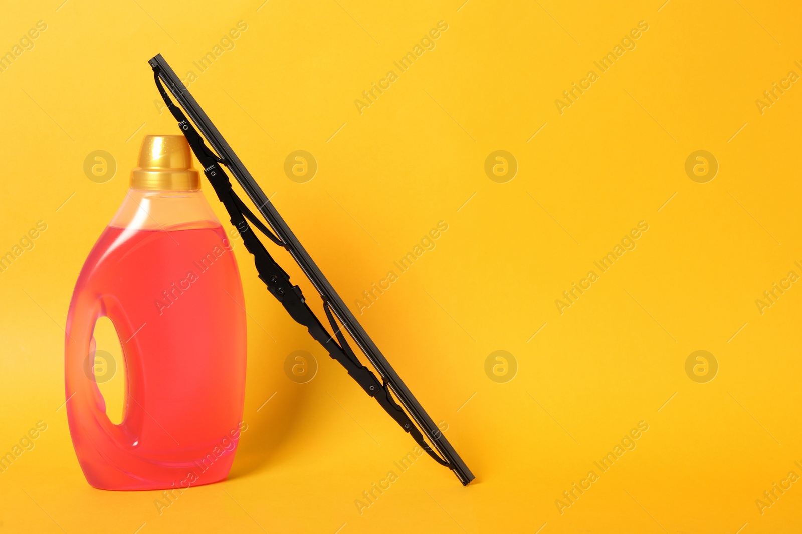 Photo of Bottle of windshield washer fluid and wiper on yellow background. Space for text
