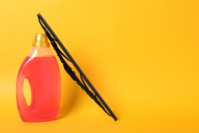 Bottle of windshield washer fluid and wiper on yellow background. Space for text