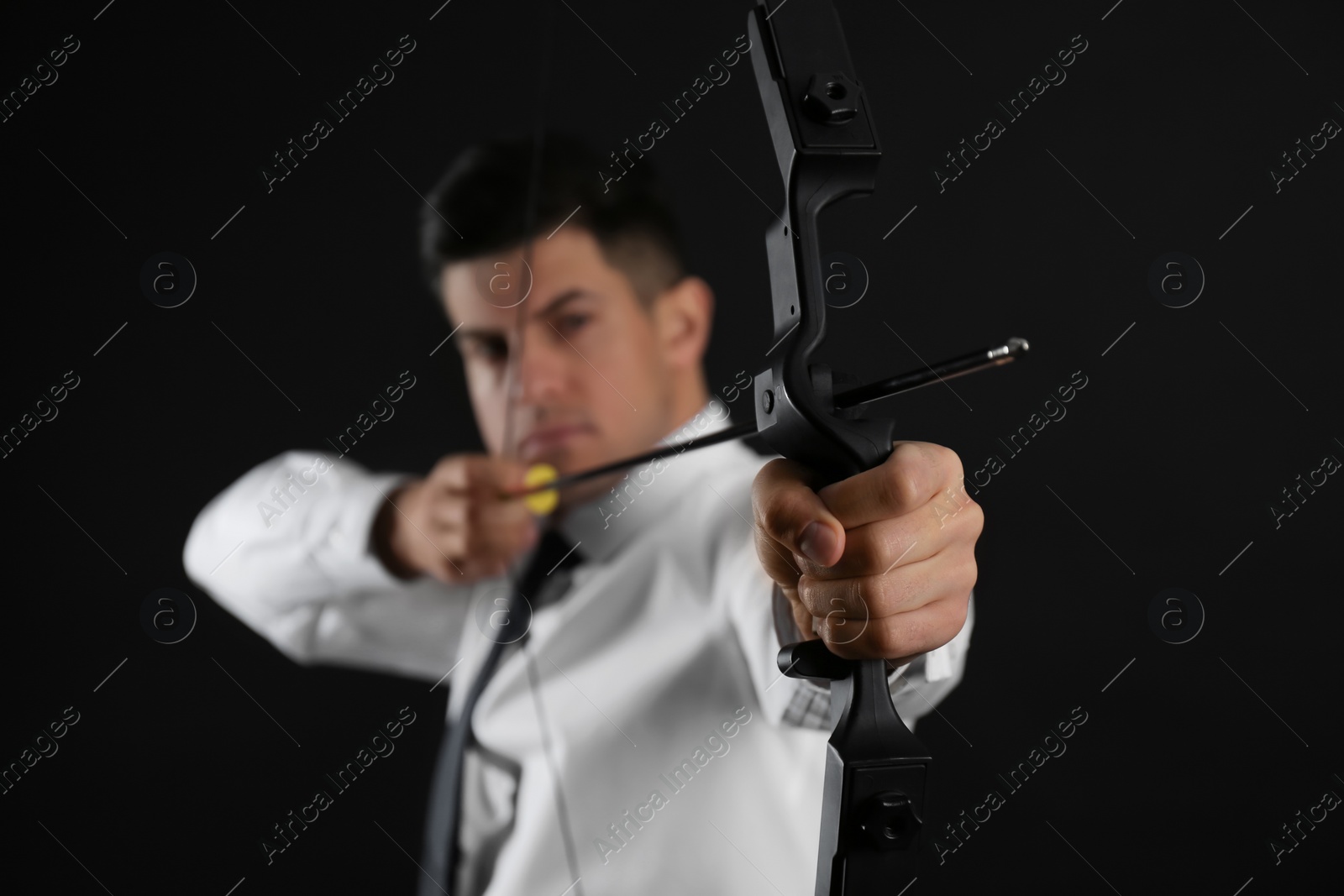 Photo of Businessman with bow and arrow practicing archery against black background, focus on hand
