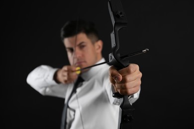 Photo of Businessman with bow and arrow practicing archery against black background, focus on hand