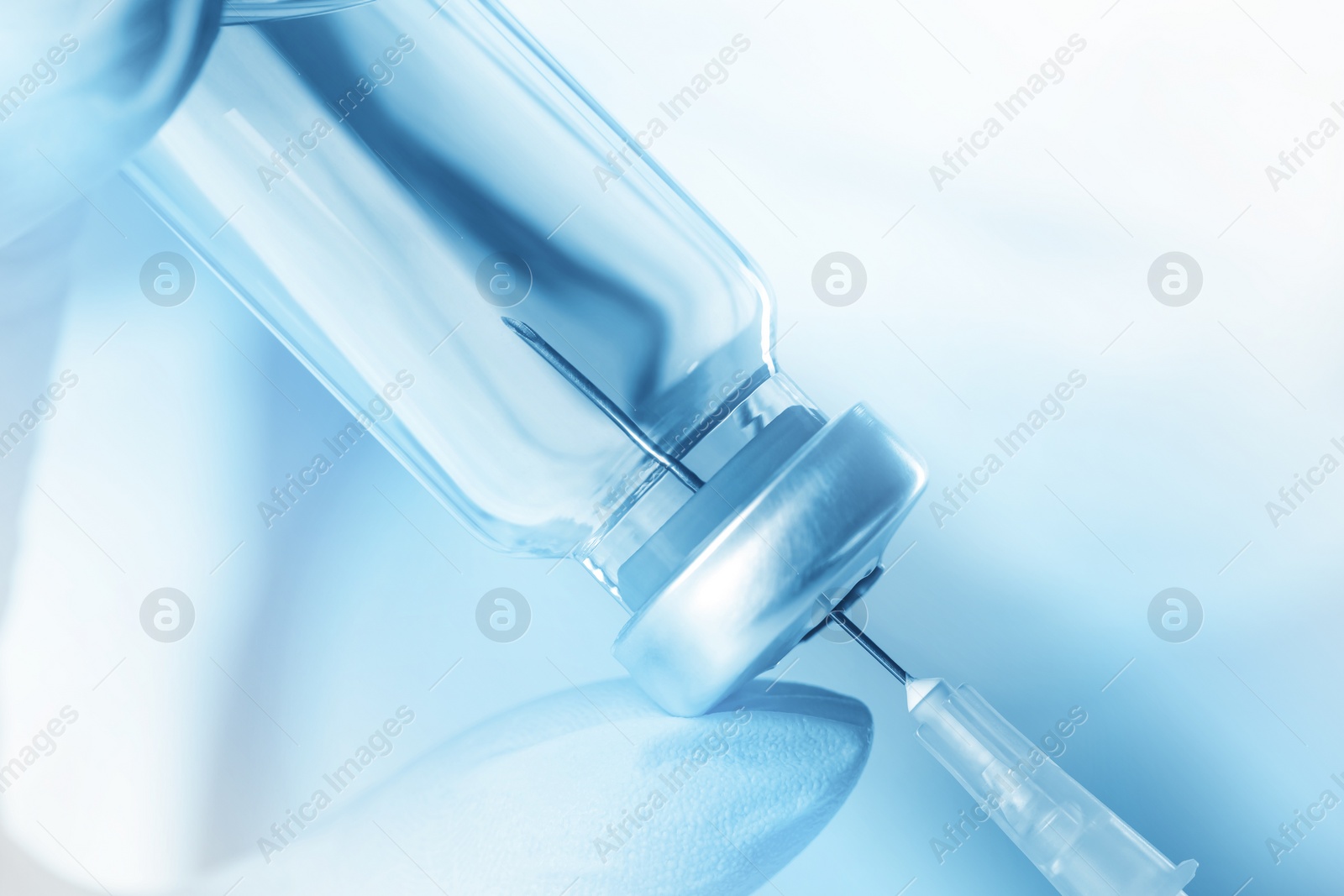 Image of Doctor filling syringe with medication from vial, toned in light blue