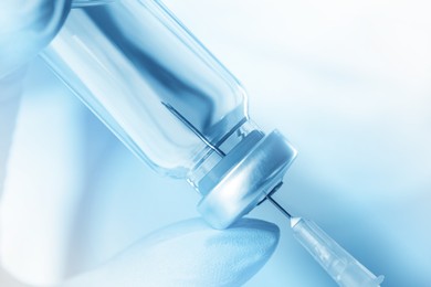 Doctor filling syringe with medication from vial, toned in light blue