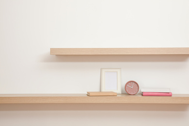 Photo of Wooden shelves with books, photo frame and clock on light wall