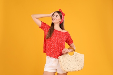 Beautiful young woman with stylish straw bag on yellow background