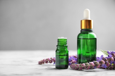 Photo of Bottles of sage essential oil and flowers on marble table, space for text