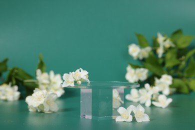 Photo of Presentation of product. Glass podium and beautiful jasmine flowers on green background, space for text