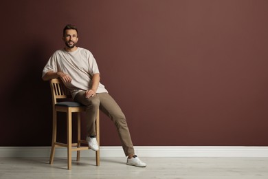 Photo of Handsome man sitting on stool near brown wall. Space for text
