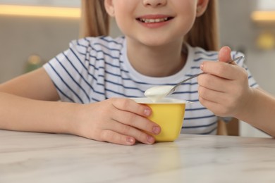 Photo of Cute little girl with tasty yogurt at white marble table, closeup