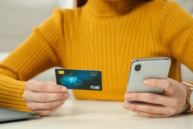 Woman with credit card using smartphone at white table, closeup